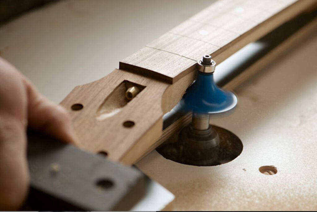 A woodworker shaping a guitar neck with a router.