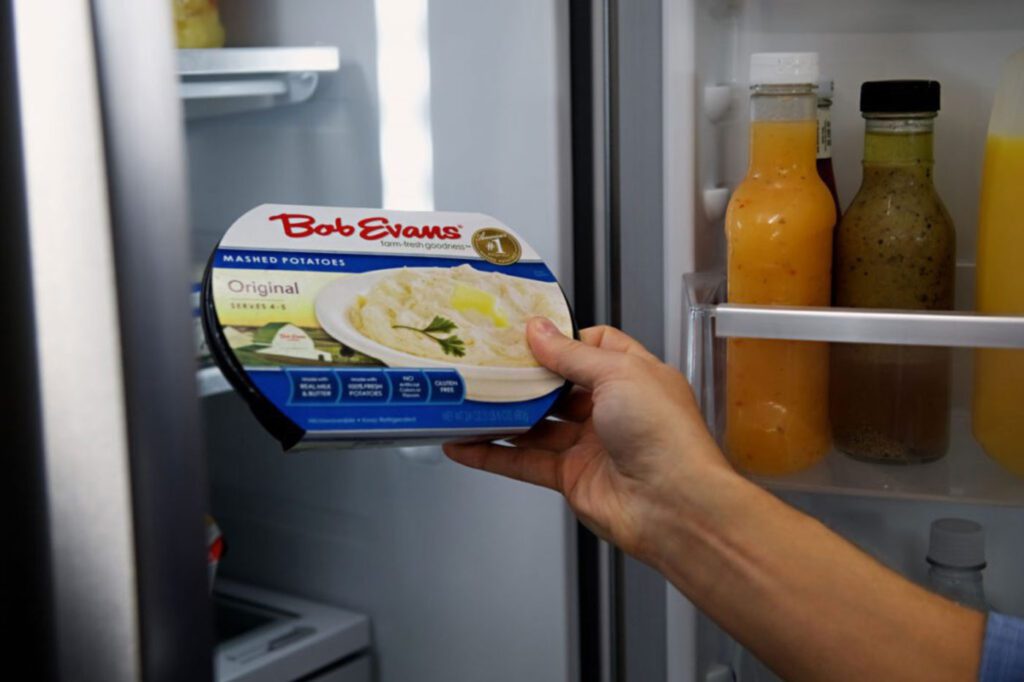 A hand holding a container of Bob Evans mashed potatoes.