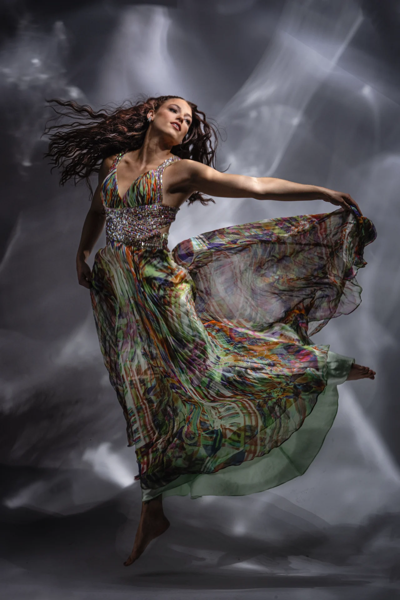 A woman gracefully dances in a flowing, colorful dress against a dramatic smoky background.